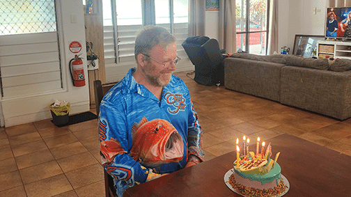 Simon smiling at a birthday cake with candles at a Bluegum SIL home.
