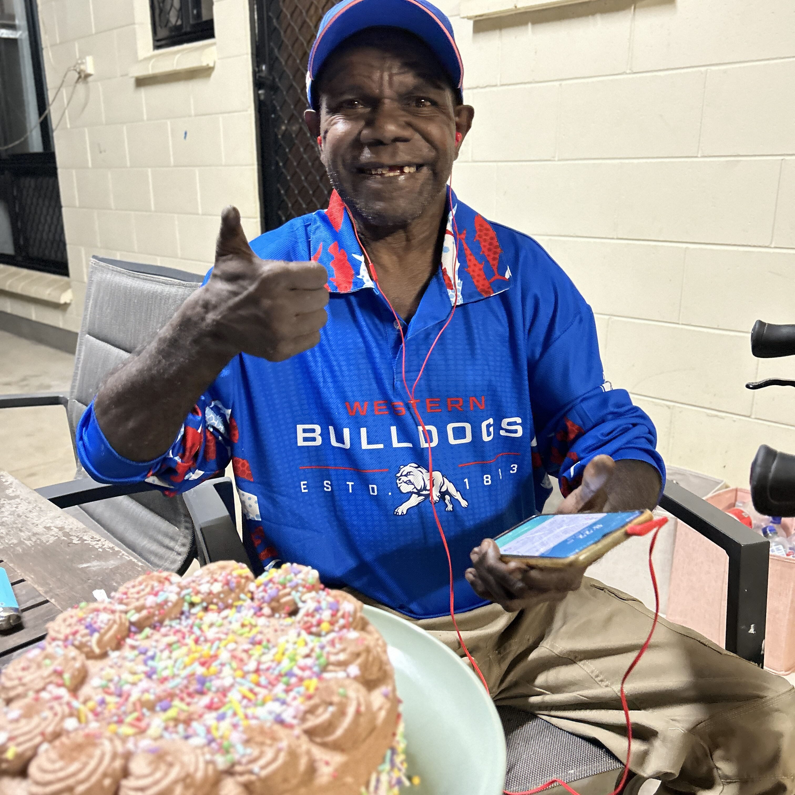 Nathaniel giving a thumbs up next to a chocolate birthday cake while on respite in Darwin.