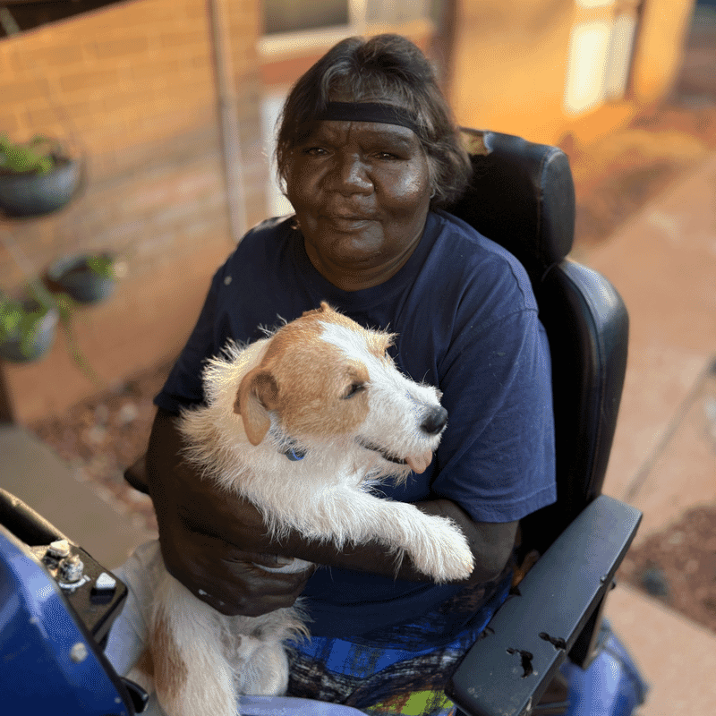 Cynthia in her power chair holding her dog at home in Tennant Creek.